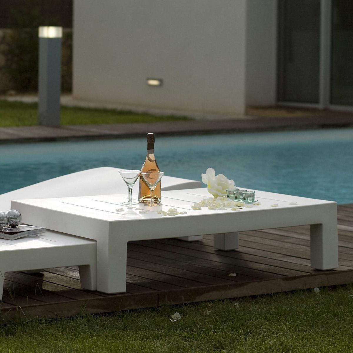 Modern Square Plastic Side Table — White outdoor table with wine bottle, glasses, and décor by a pool.
