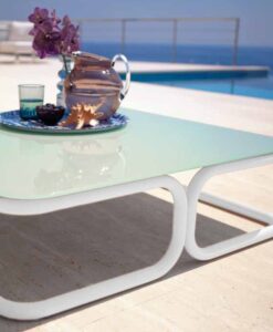A glass teapot and cup on a modern traditional coffee table by a pool, with a sea view in the background.