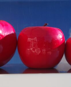 Four glossy red apples of different sizes set against a backdrop of blue sky and clouds