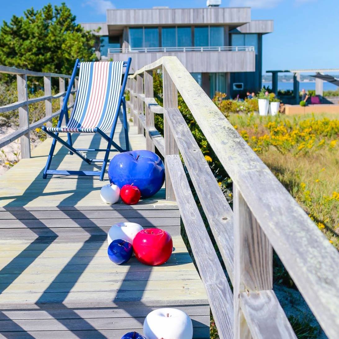 A boardwalk with a striped chair and colorful apples leading it's way to a modern house