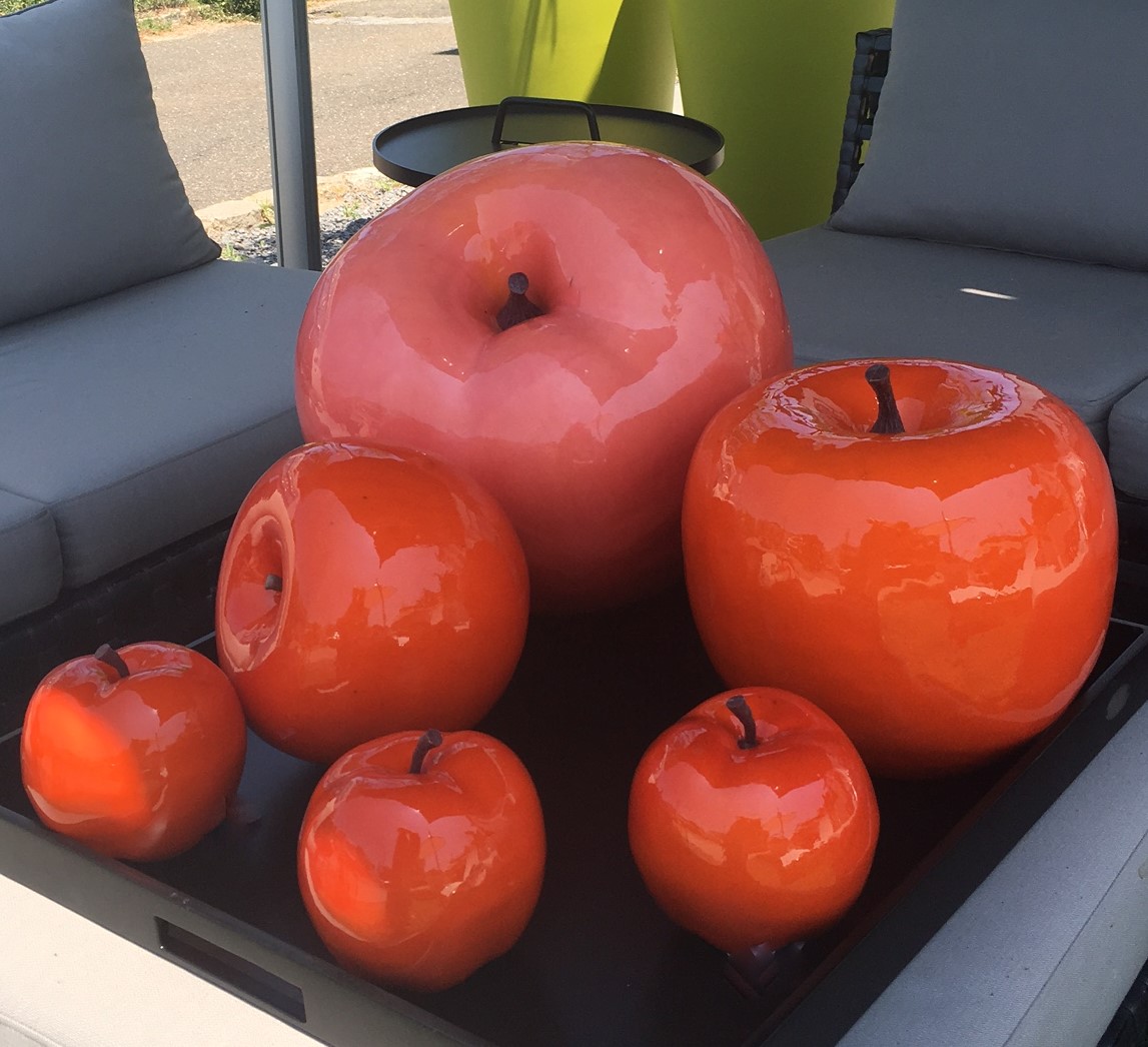 Shiny oversized artificial apples are on a table, including one large apple and several smaller ones.