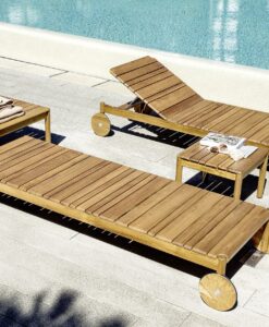 Code Teak Chaise Lounger —Wooden poolside loungers and table with towels and magazines, next to a pool.