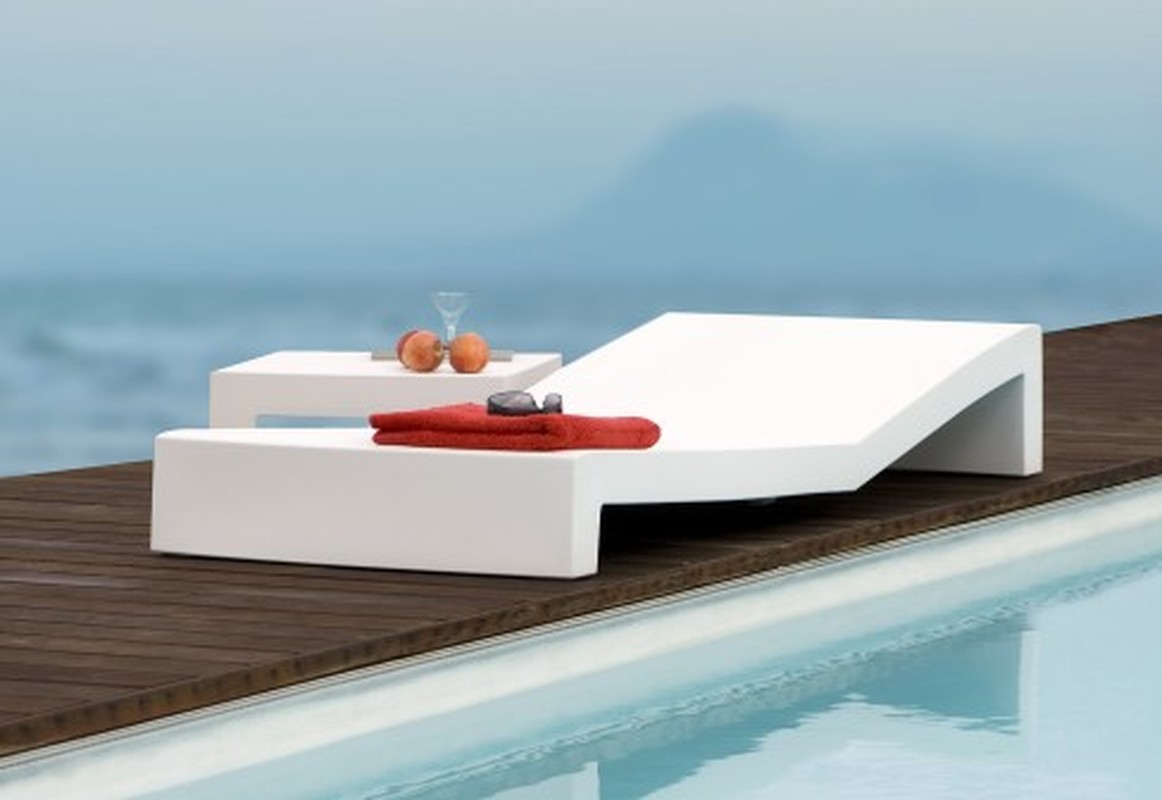 Rectangular White Chaise lounger —Modern white sun lounger by a pool with a towel, sunglasses, and a cocktail on a side table.