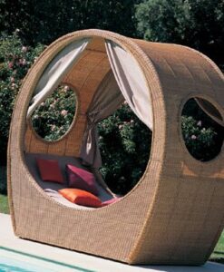 Moon Traditional Daybed — Wicker outdoor pod chair with cushions by a pool, curtains partly open.