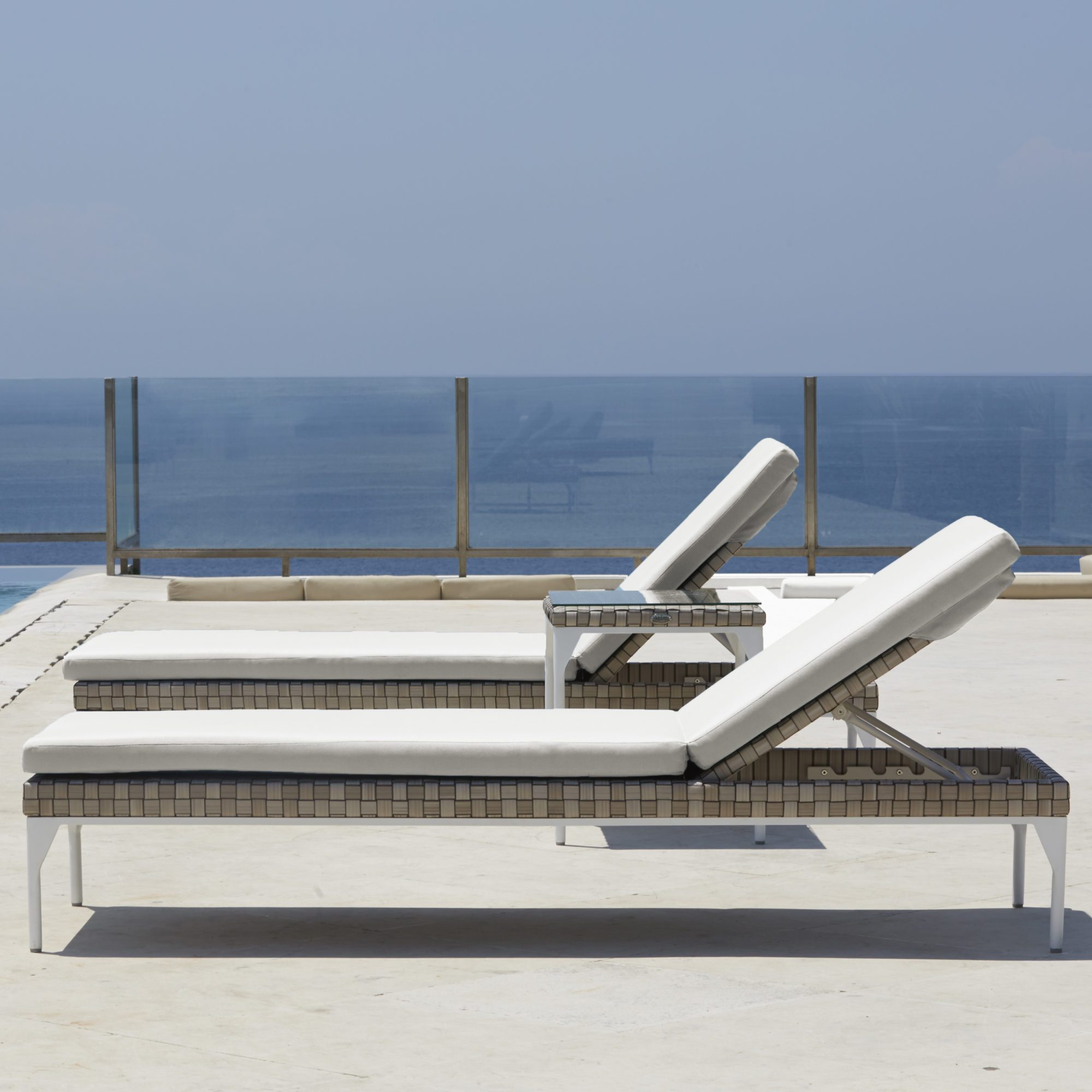 Chaise Lounger — Two white sun loungers by a pool overlooking the sea.