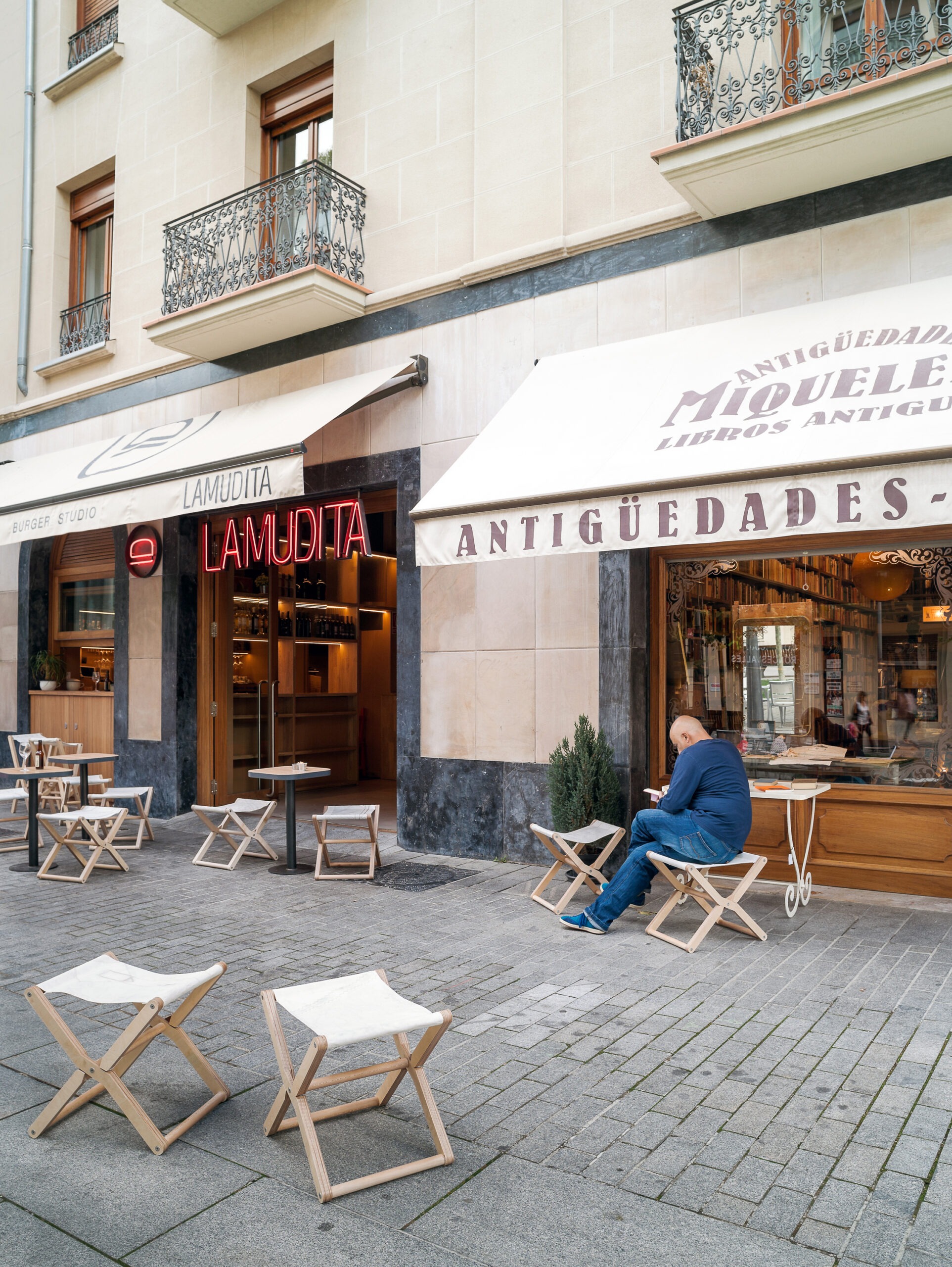 Person sitting on a director's chair outside a shop with tables and stools