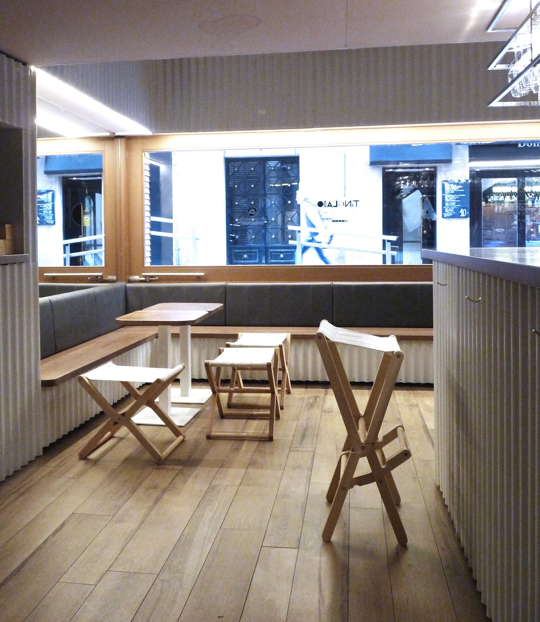 Modern cafe interior with wooden tables, folding stools, and large windows.