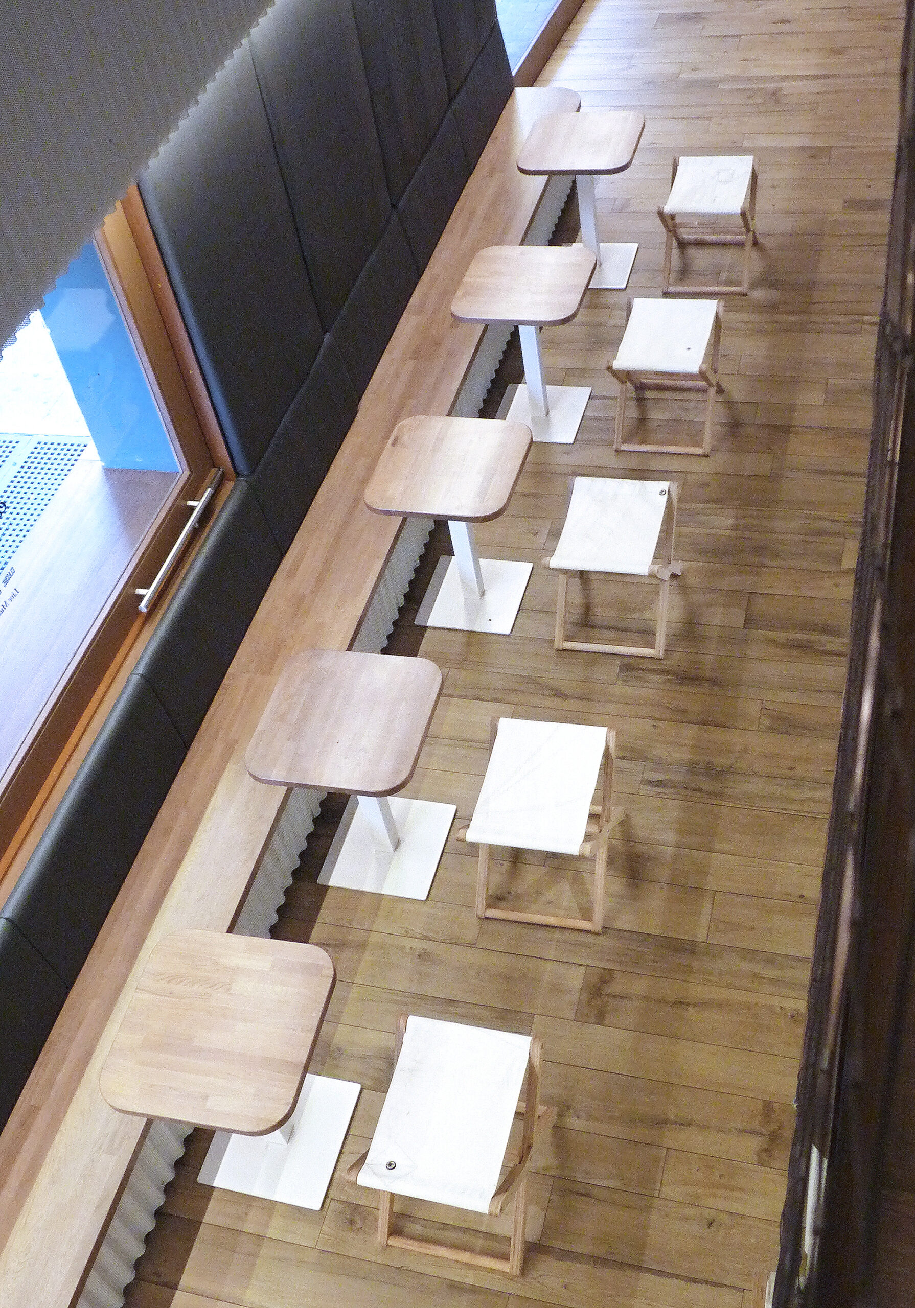 An overhead view of a row of modern low Stools and tables on a wooden floor.