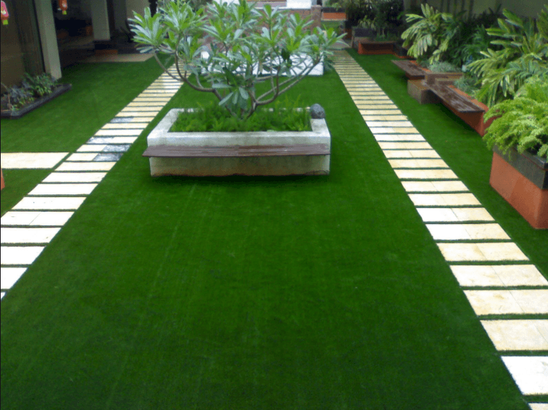 An indoor garden featuring artificial green grass and a stone pathway surrounded by potted plants.