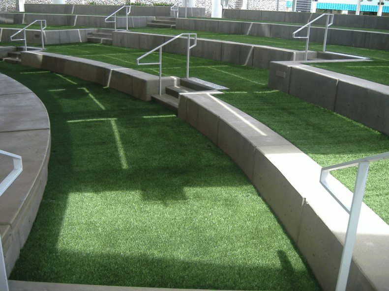 Outdoor amphitheater with steps covered in artificial grass, concrete edges, and metal handrails on the sides.