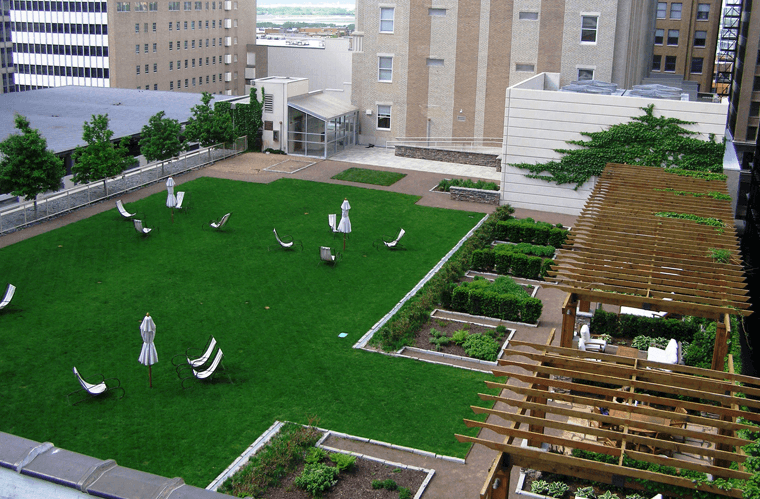 Urban rooftop garden with artificial green grass, plants, benches, and a pergola