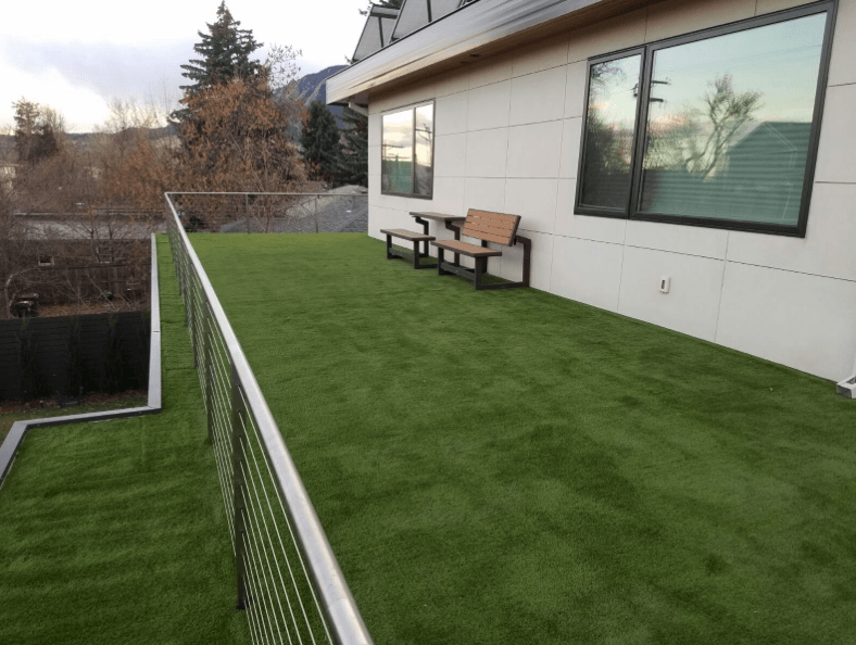 An outdoor terrace with lush green artificial grass and a wooden bench positioned against a building wall