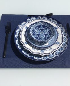 Blue and white floral melamine plates, stacked on a dark blue placemat, with a black fork on the left, spoon on top, and knives beside.