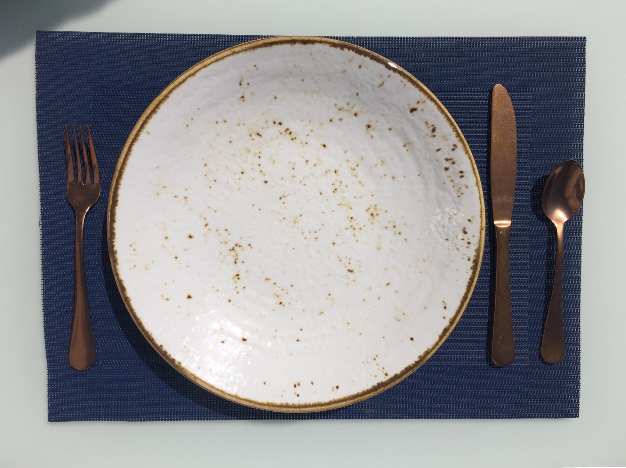 On the table mat, an empty, used white plate with crumbs, a knife and spoon on the right side, and a fork on the left side.