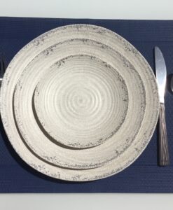 A textured ceramic plate with a knife and spoon on the right side, and a fork on the left, all placed on a blue placemat.