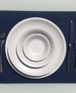 Stacked white plates and Melamine Matt White Bowls, a fork to the left, and a knife to the right on a blue mat.