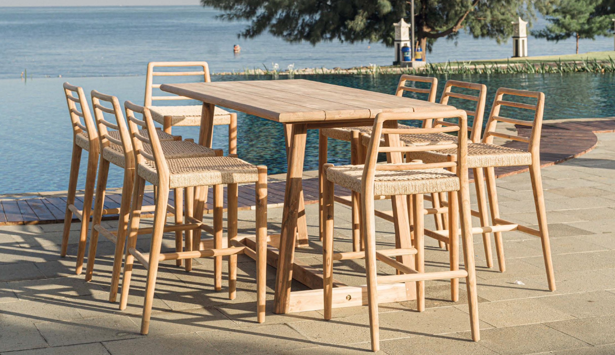 Collem bar — Outdoor wooden dining table and chairs by the sea, with trees