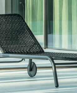 A modern wicker lounge chair on a sunny patio with glass doors and sheer curtains.
